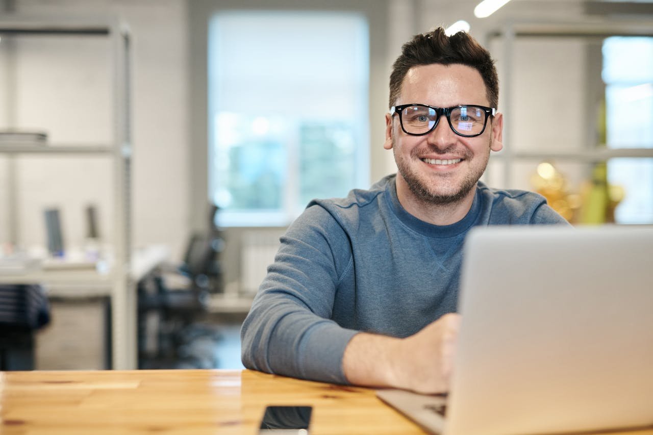 The Art of Drawing Readers In: Your attractive post title goes here Happy man wearing glasses working remotely on laptop in modern office environment.
